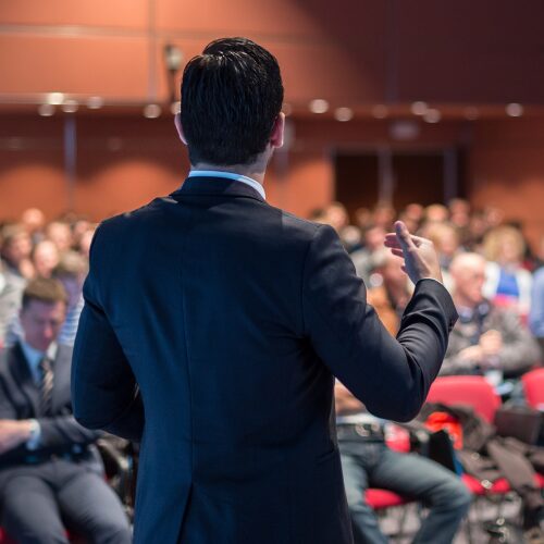 A man in a suit with his back to the camera as he speaks with a group of people