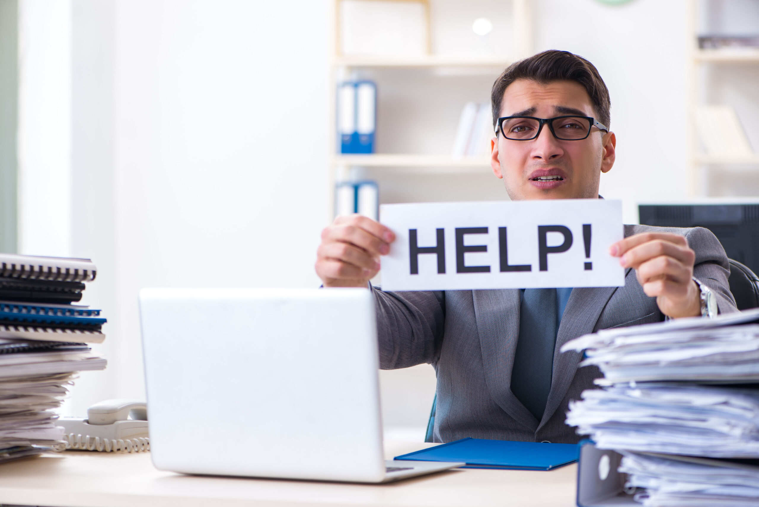 a man sitting at a desk holding up a sign that reads "help"