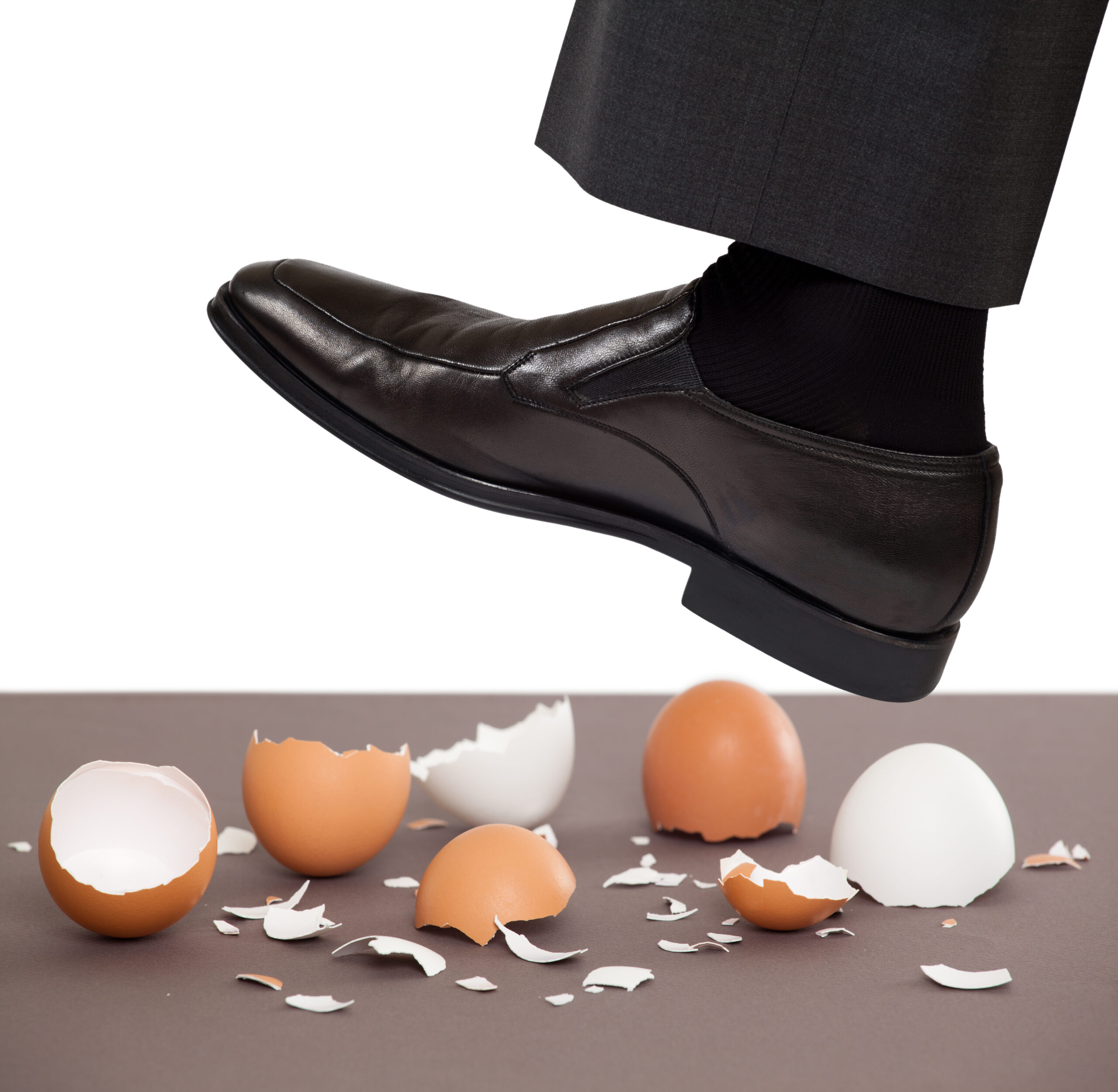 a dress shoe hovering over, about to step on, smashed eggshells