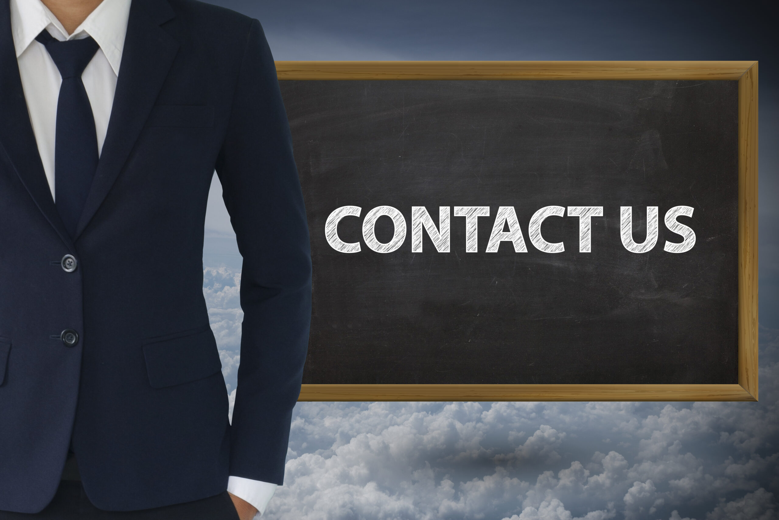 A businessman's torso is standing next to a chalkboard with "Contact Us" written.