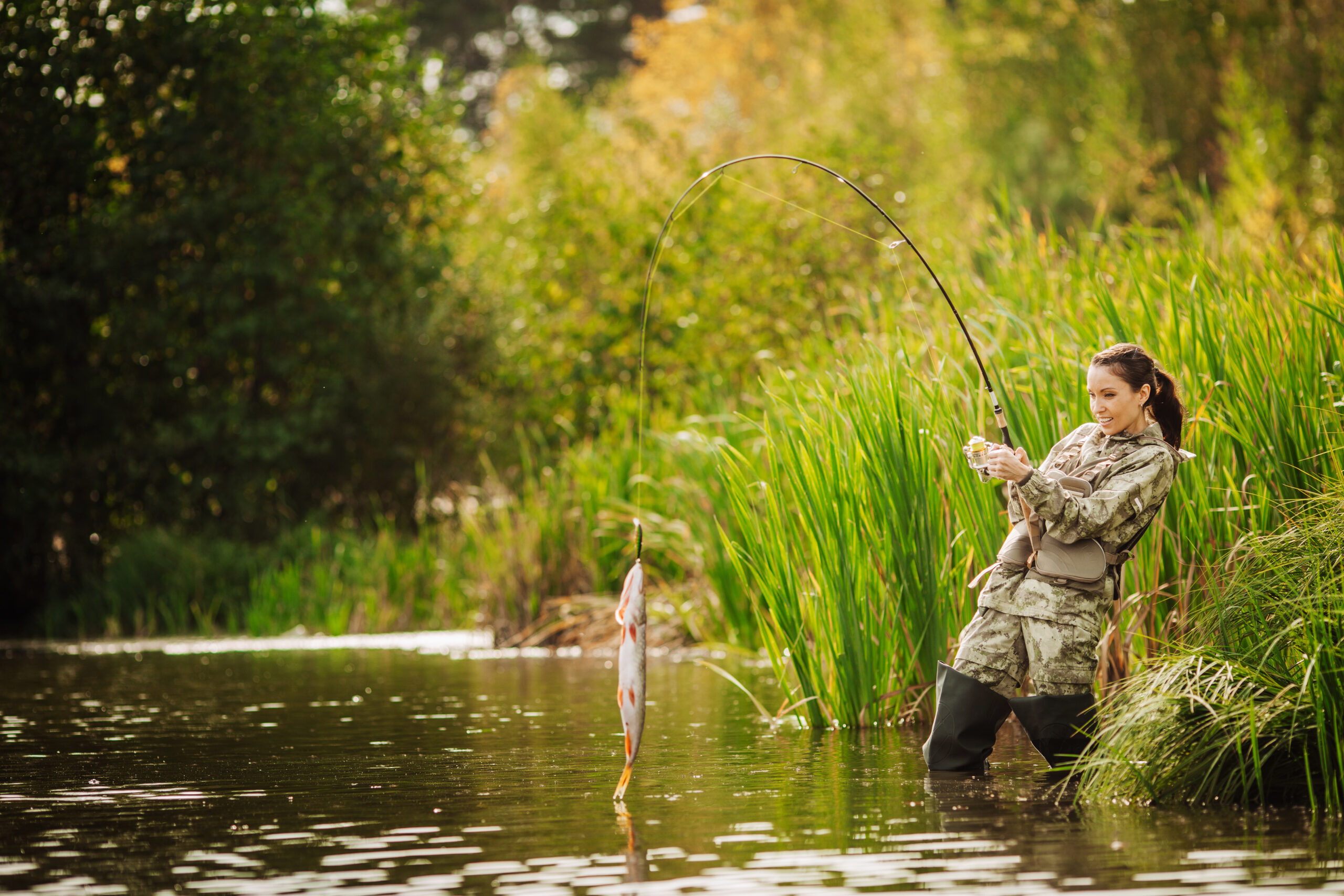 a woman fishing in a pond in the middle of reeling in a fish